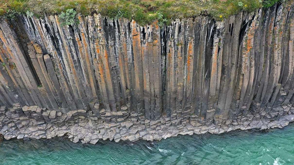 A long wall of upright basalt columns rising straight out of the turquoise river at Stuðlagil