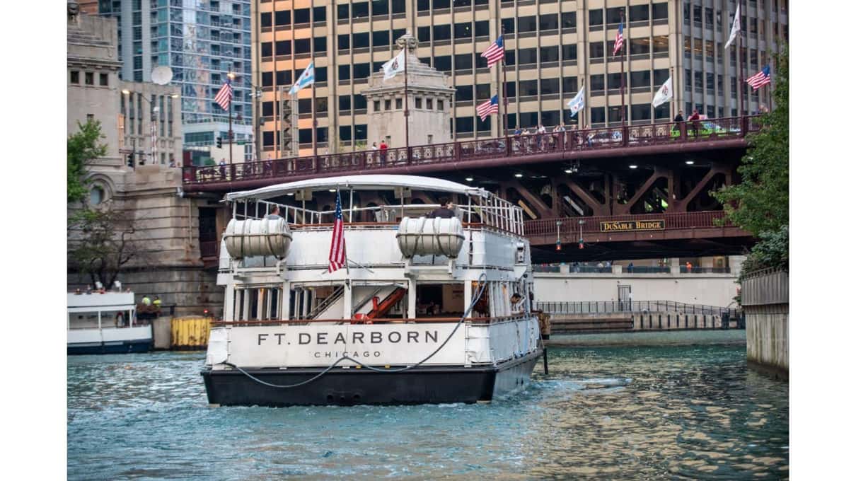 A white Chicago Line tour boat with an open upper deck moored beside the river walkway