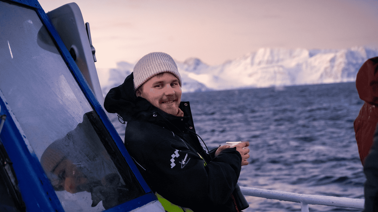 A smiling crew member in a beanie standing on a boat deck in the winter cold