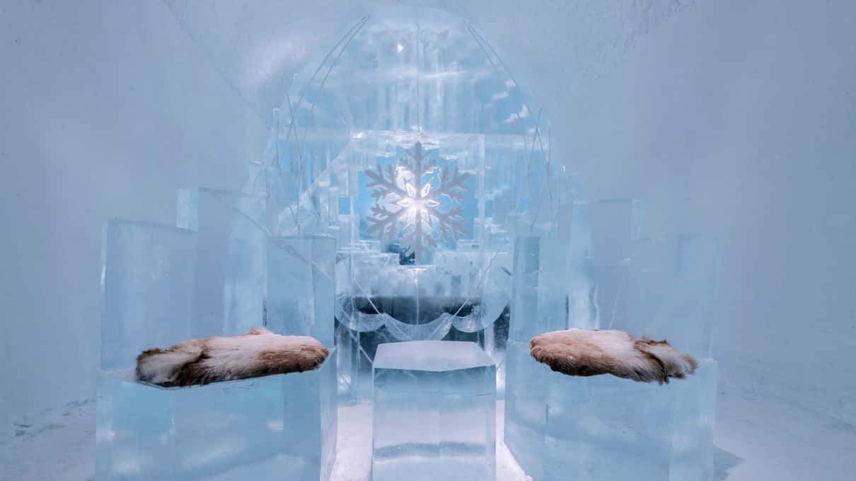 Two ice chairs with reindeer-fur seats in front of a carved ice wall with a crystal at its center