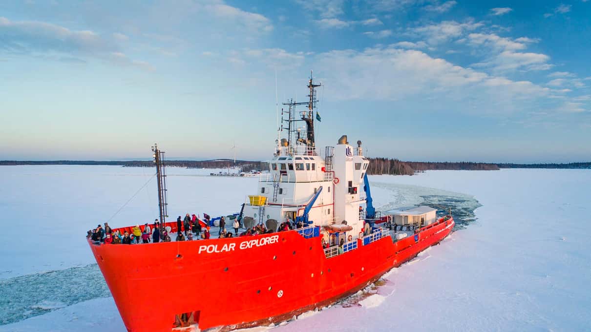 The red-hulled Polar Explorer pushing through white sea ice with passengers lining its decks