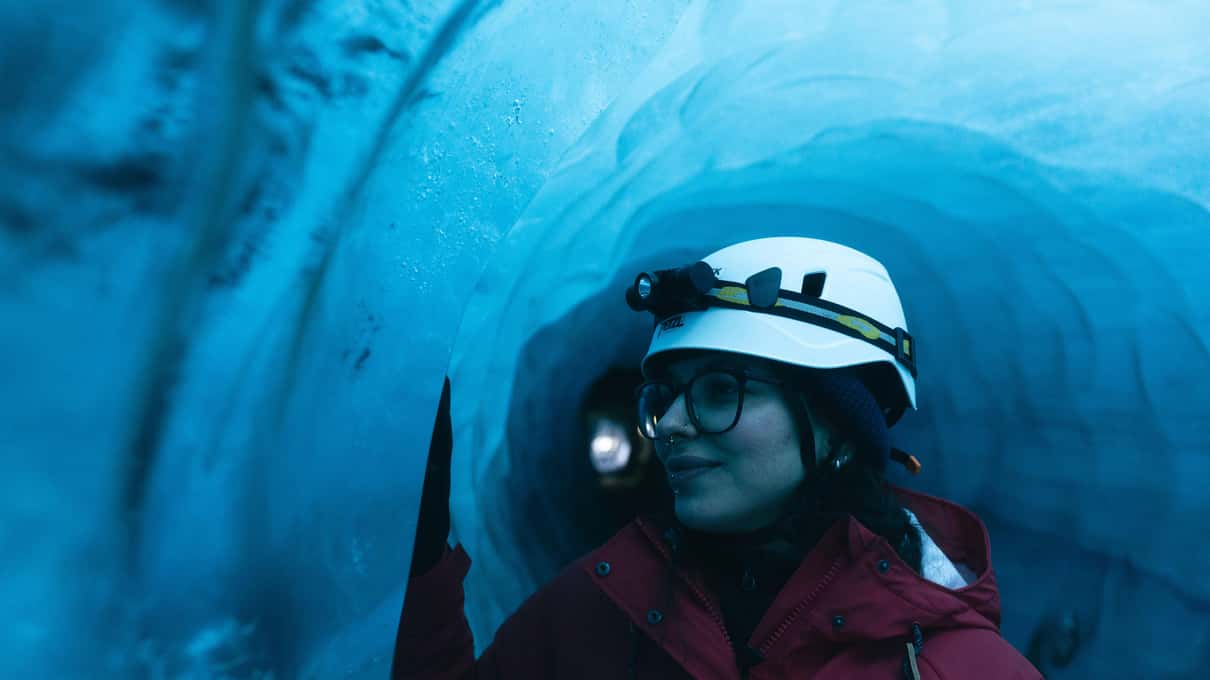 Ein Besucher mit weißem Helm und Stirnlampe in einer blauen Eishöhle auf einer Tour von Katlatrack