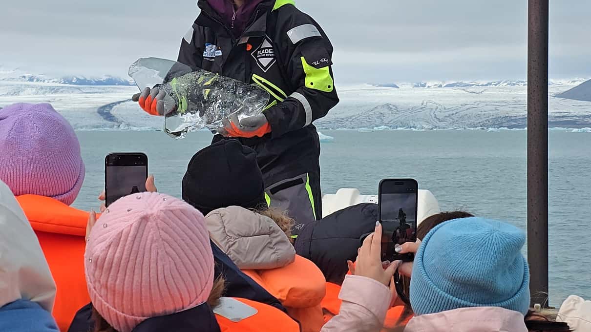 Guide holding a clear piece of glacier ice for passengers in orange life jackets on a Jökulsárlón boat tour