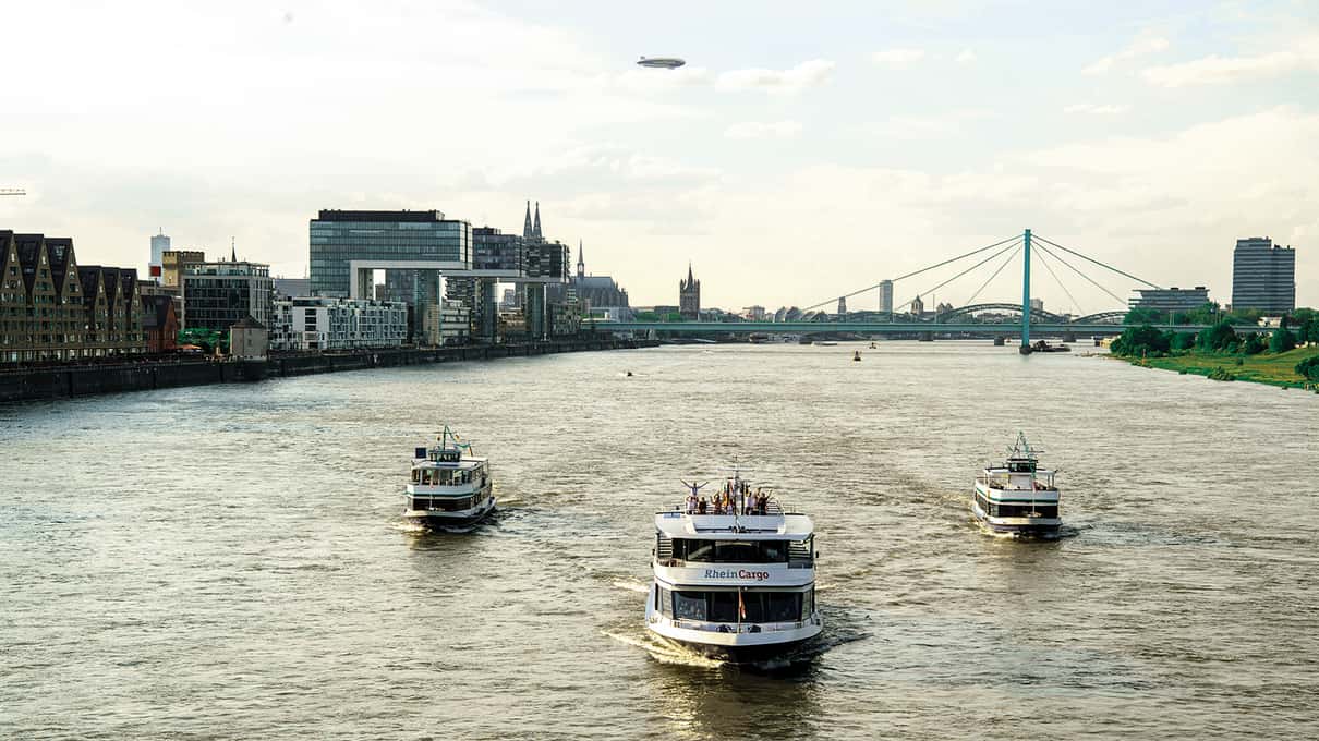 Three passenger boats on the Rhine in Cologne with a cable bridge behind them