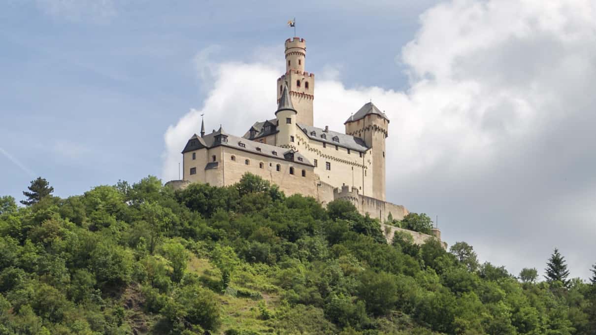 The pale walls and slender tower of a hilltop castle above the Rhine near Koblenz, under white clouds
