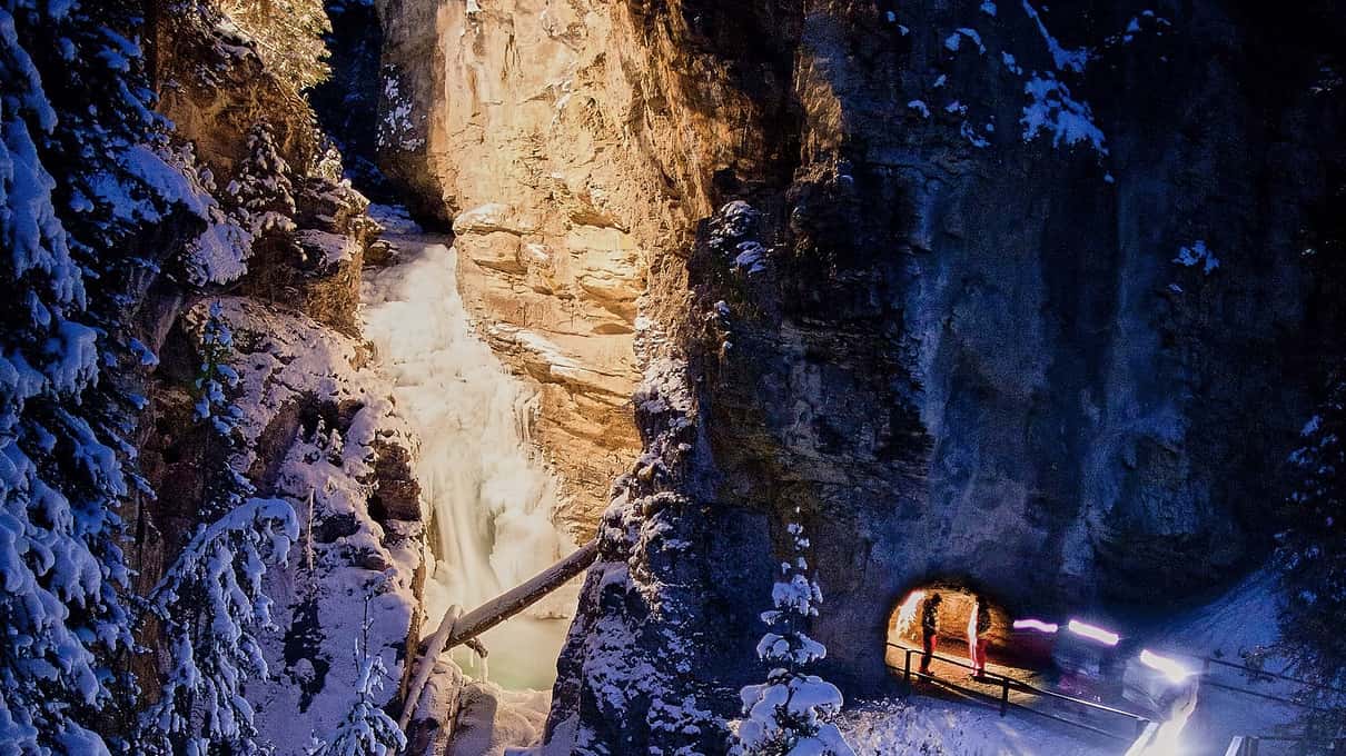 Headlamps lighting a catwalk beneath a frozen waterfall inside Johnston Canyon at night