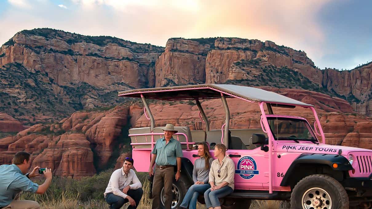 A pink open-top jeep on a dirt track below the red spires of Thunder Mountain in Sedona