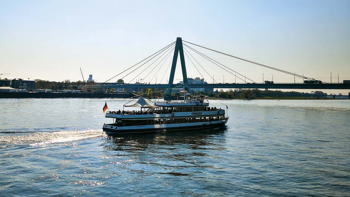 A white sightseeing boat passing under the Severin Bridge on the Rhine in Cologne