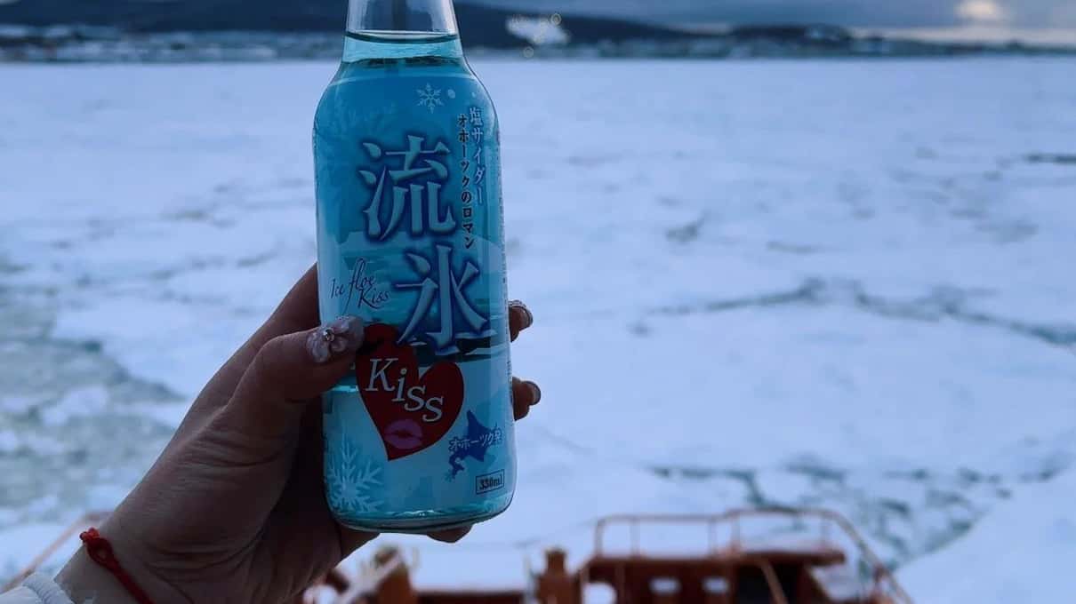 A hand holding up a blue bottle of drift ice soda on the icebreaker deck above the sea ice