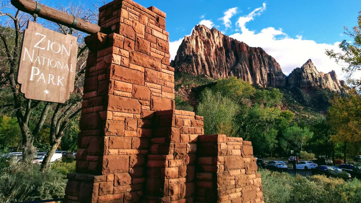 El cartel de piedra de la entrada al Parque Nacional Zion con el pico rojo del Watchman alzándose detrás