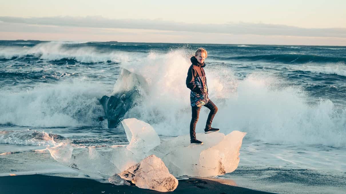 Traveler standing among glacier ice chunks on the black sand of Diamond Beach beside Jökulsárlón