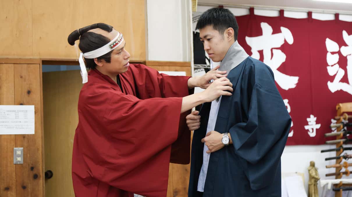 Instructora ajustando un kimono rojo a una participante antes de la clase de rodaje de lucha samurái