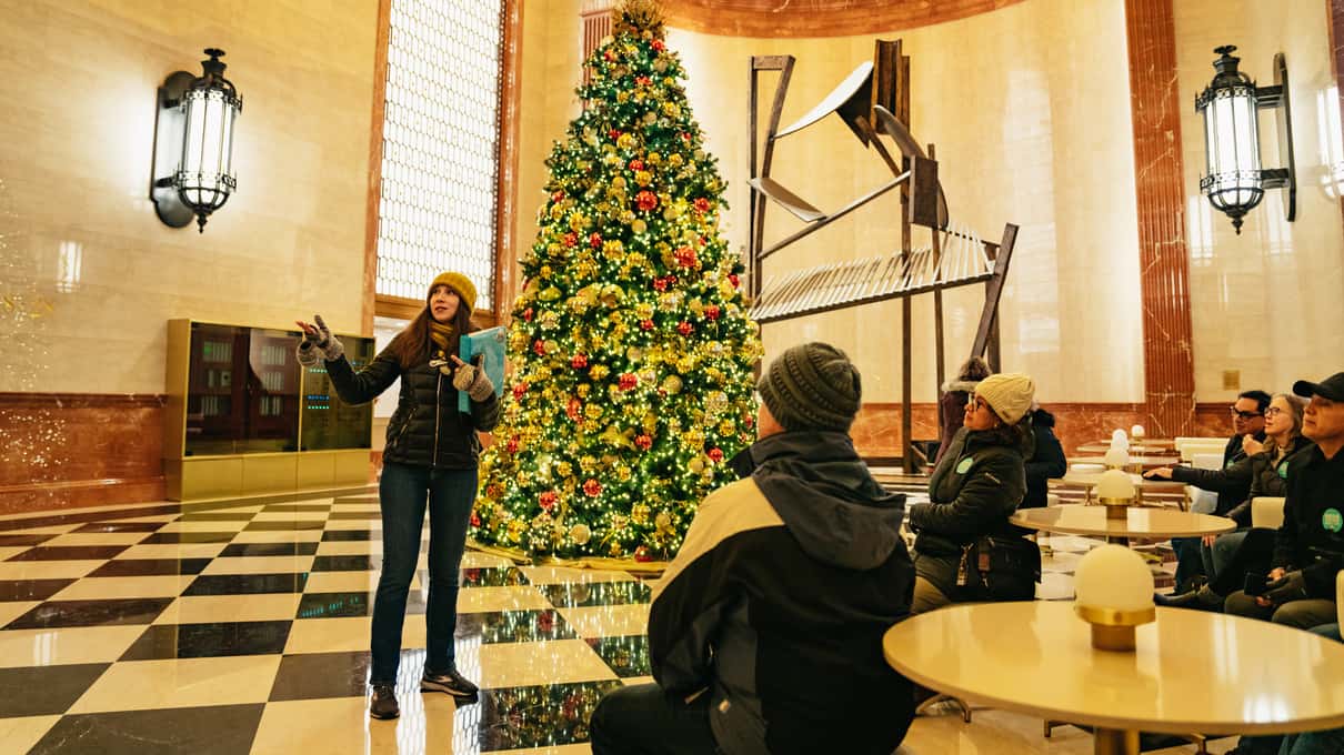 Ein Guide von Inside Chicago spricht in einer Lobby mit Schachbrettboden und Weihnachtsbaum zu einer kleinen Gruppe