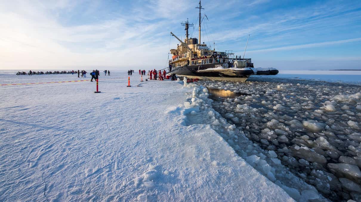 Icebreaker Sampo beside its channel of broken ice with guests standing on the frozen sea