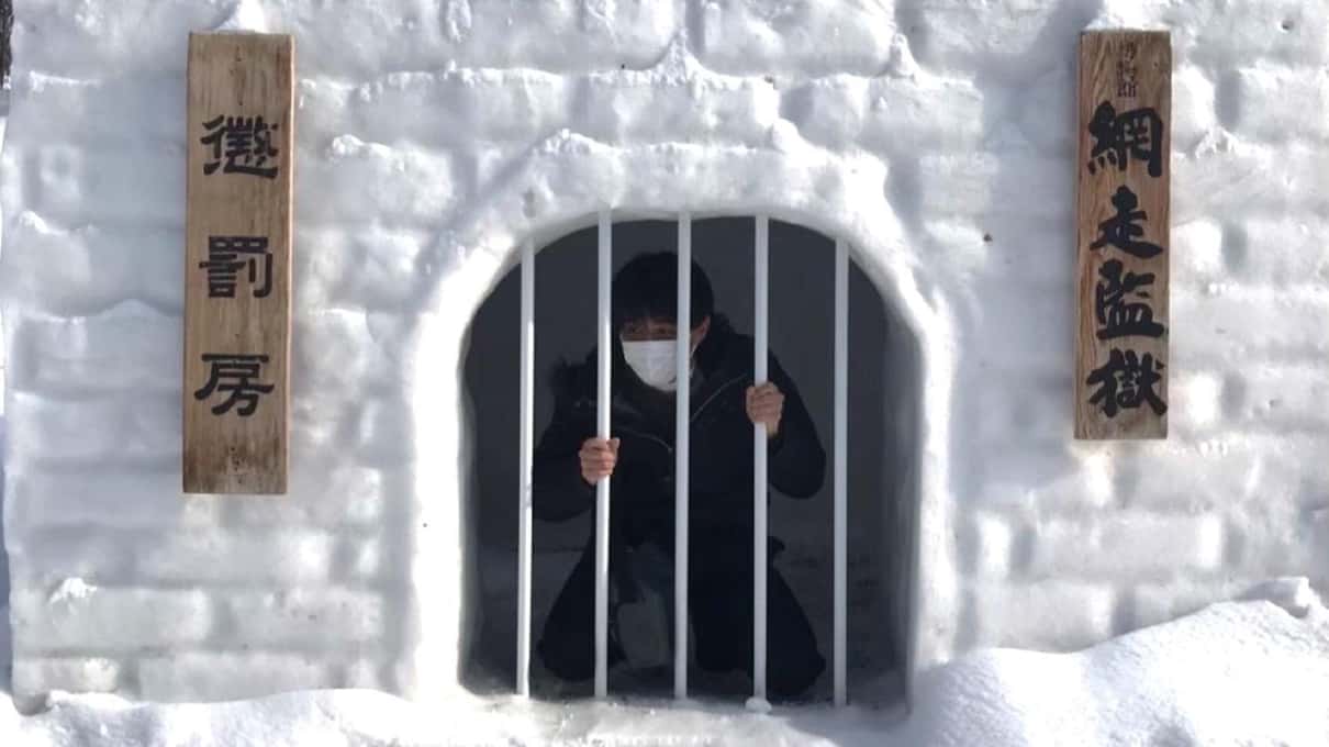 A prisoner figure looking out from behind the bars of a snow-covered cell window at the Abashiri Prison Museum
