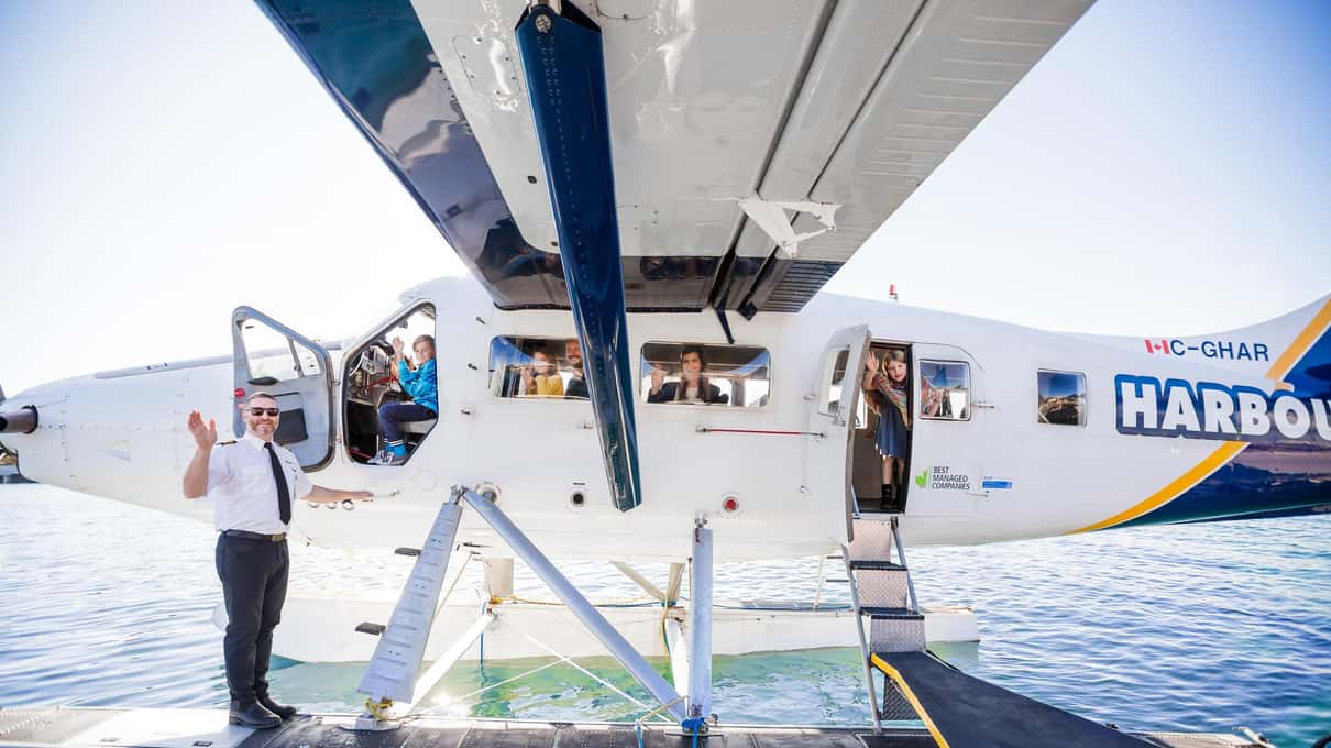A pilot in uniform waving from the float of a Harbour Air Twin Otter as passengers settle into their seats