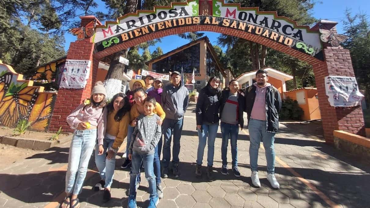 Small tour group posing together at the wooden gate of a monarch butterfly sanctuary