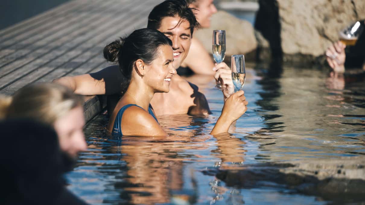 A couple sharing a drink in one of the steaming hot pools at Hvammsvik