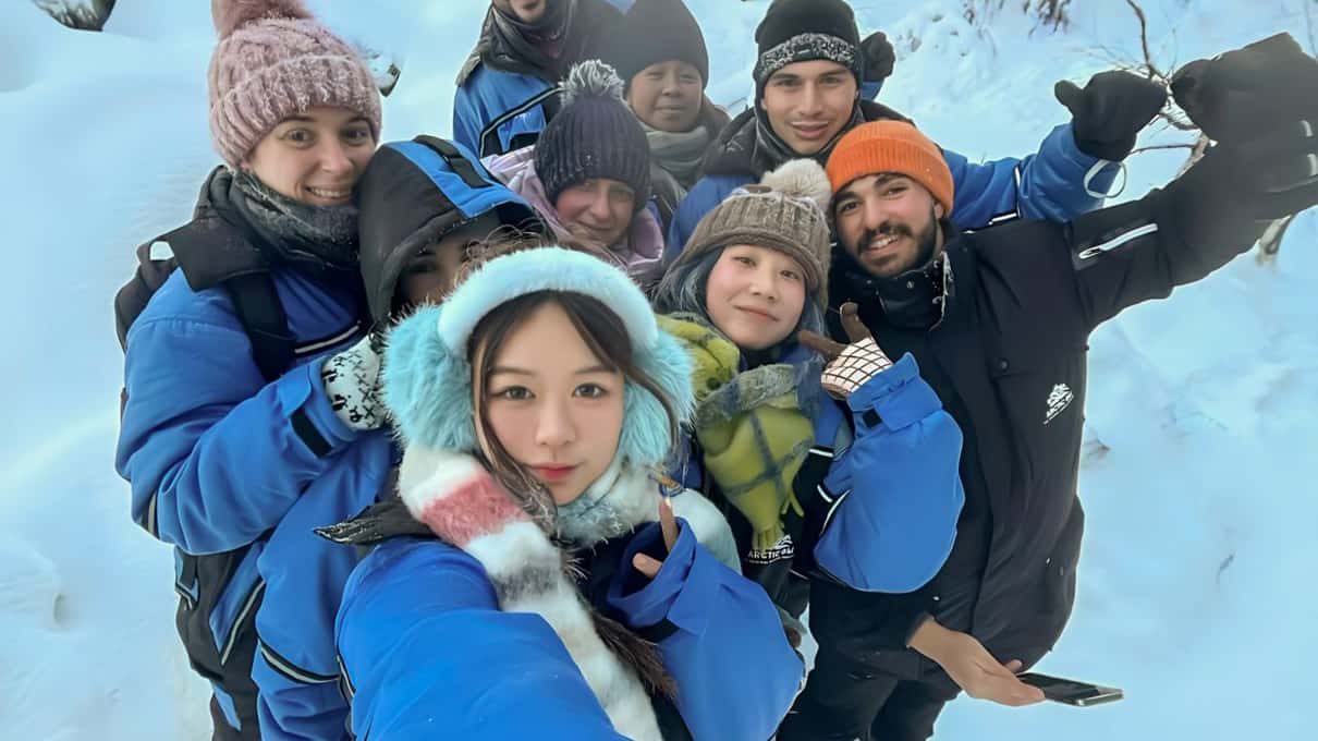 A small group of hikers in blue thermal overalls taking a selfie together in deep snow