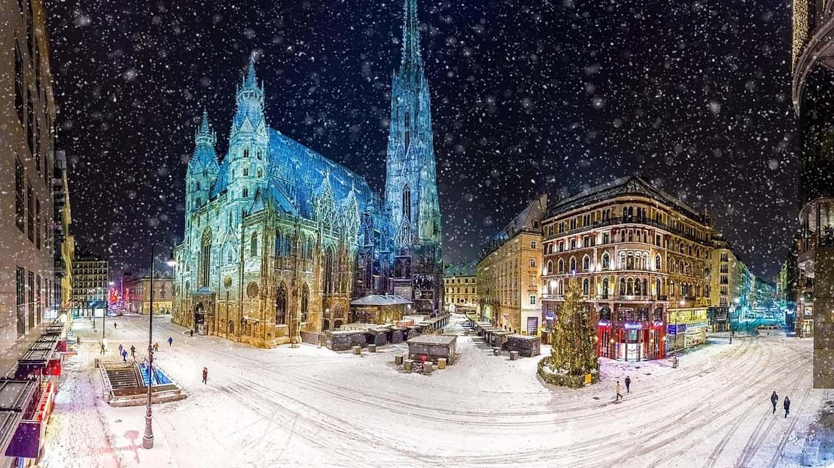 St. Stephen's Cathedral lit up at night in falling snow, with the square in front of it covered in white