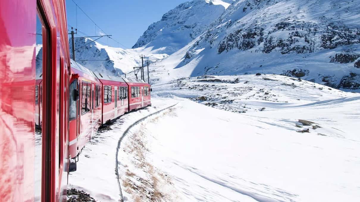 The red Bernina train in a snow-covered valley with white peaks behind
