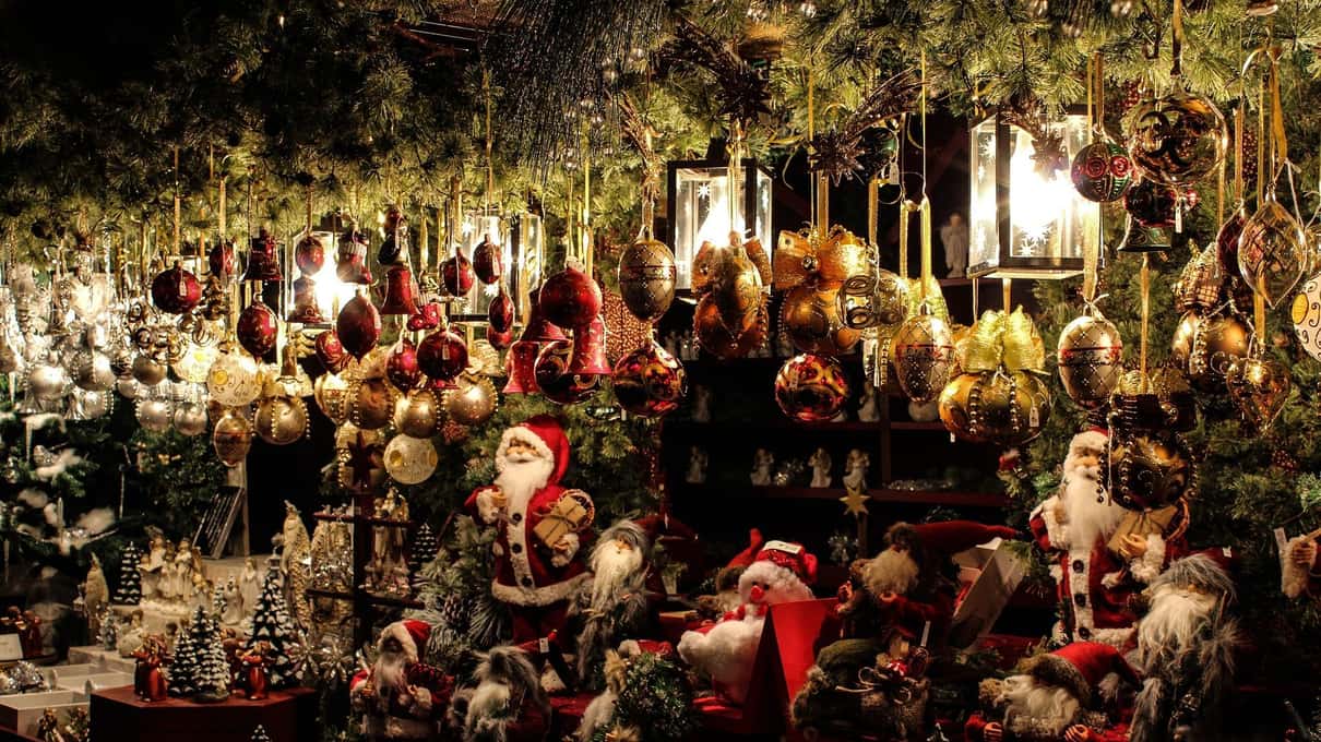 A Christmas market chalet at night crowded with red and gold ornaments, little Santa figures and fairy lights