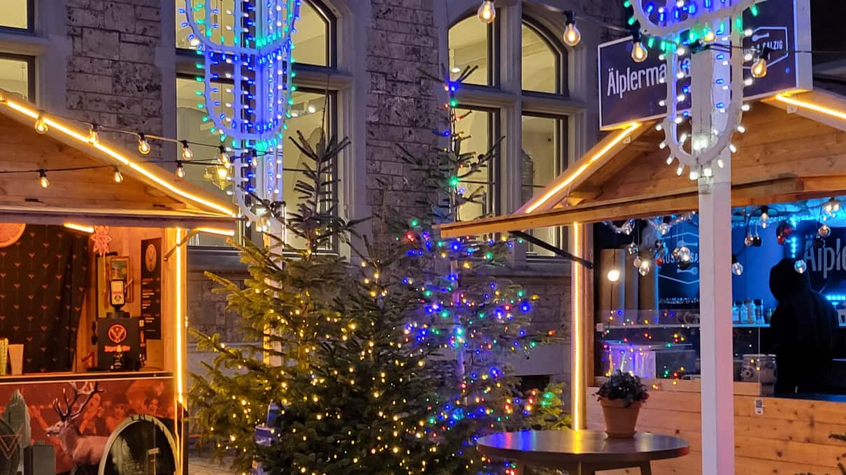 Wooden Christmas market huts strung with fairy lights and small fir trees beside an old stone building in Zurich
