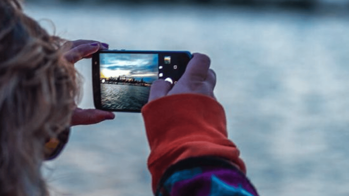 A hand holding up a phone to photograph the Chicago skyline from the deck of a river cruise boat