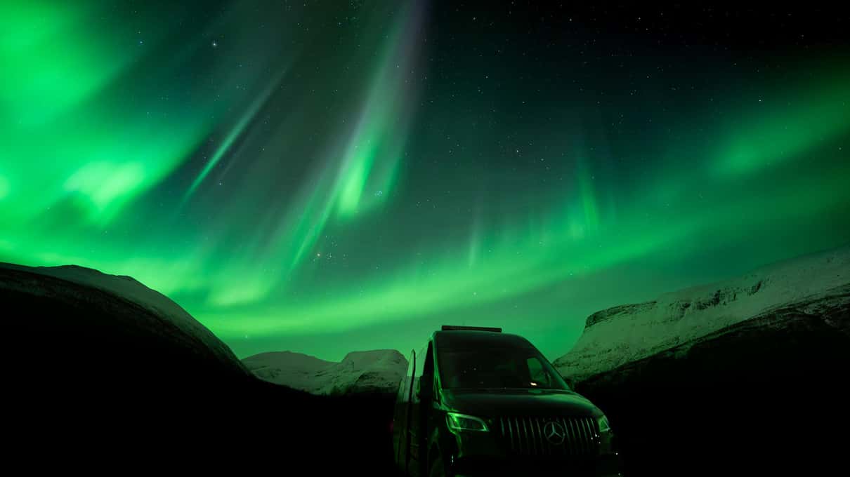 Aurora verde muy intensa sobre un vehículo aparcado en una carretera nevada, de noche