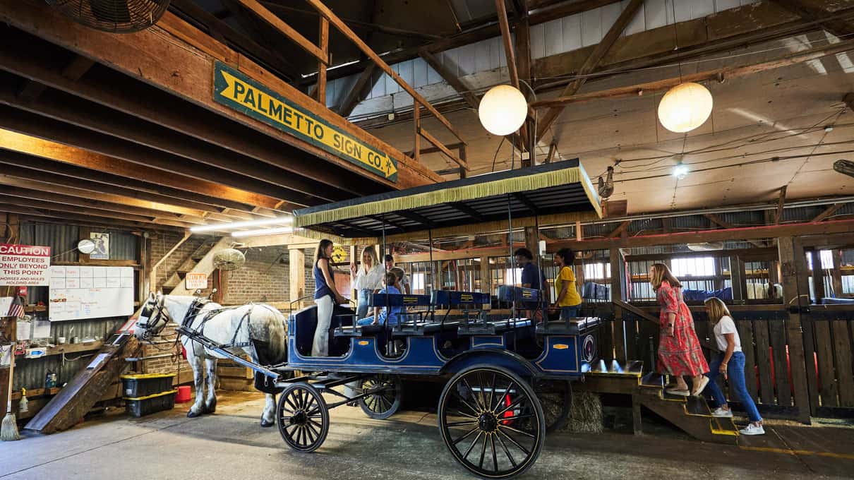 Riders stepping into a blue Palmetto carriage from the raised boarding platform inside the Big Red Barn