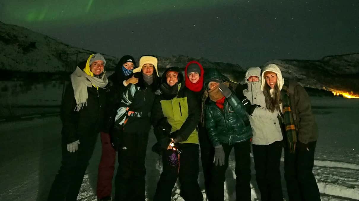 A small group in winter coats and hats posing at night with a faint aurora above them