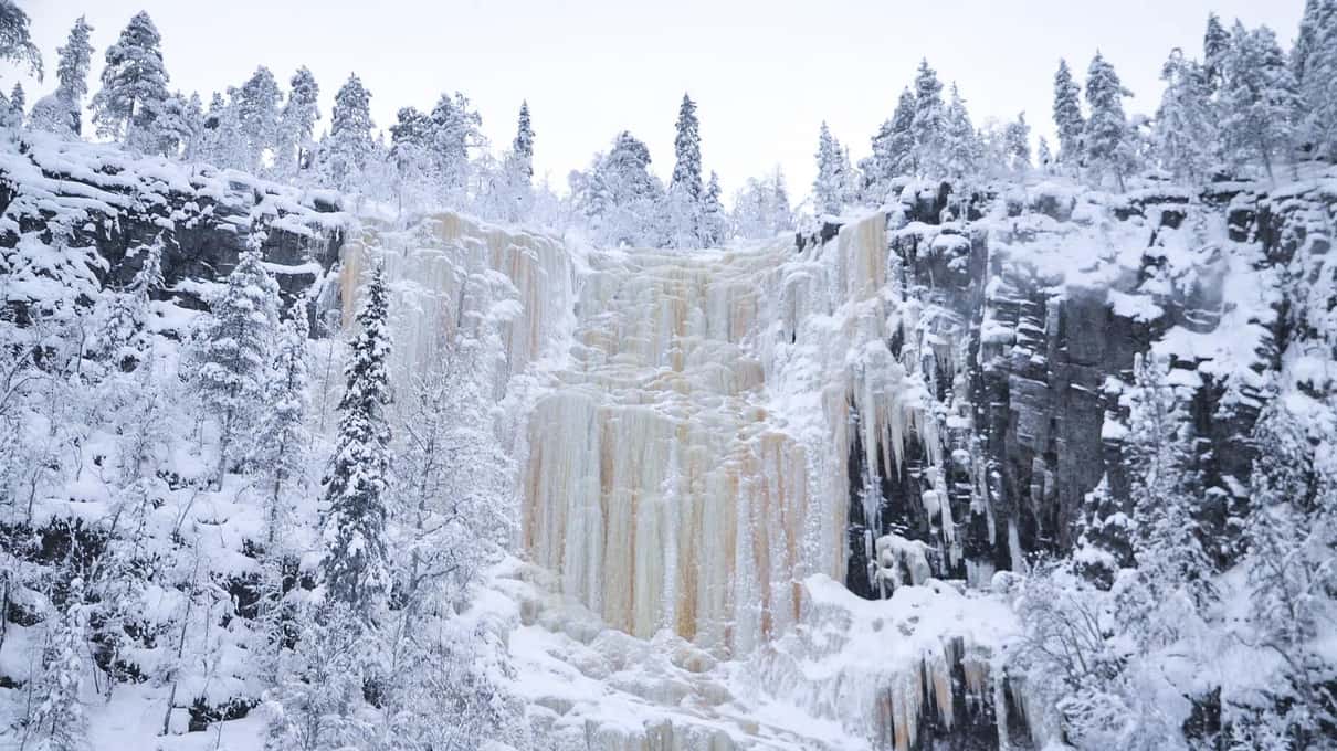 A wide wall of white and amber ice between snowy cliffs in Korouoma canyon