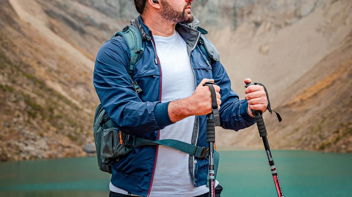 A hiker in a warm jacket walking a mountain trail with a pair of trekking poles