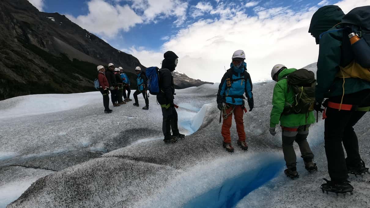 Trekkers in rain jackets and helmets walking past a deep blue crevasse on Perito Moreno Glacier