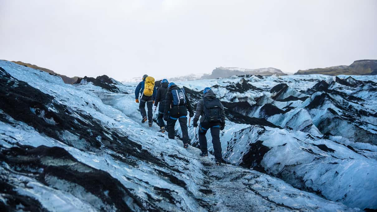 A line of hikers in crampons crossing the ash-streaked ice of the Sólheimajökull glacier