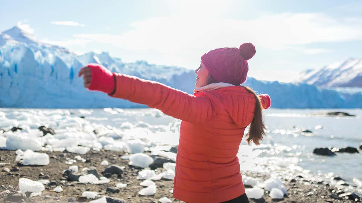 A child in a red jacket standing with arms wide on the beach in front of Perito Moreno Glacier