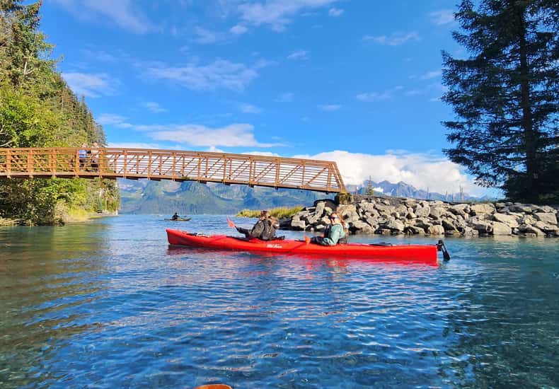 Rotes Kajak auf türkisfarbenem Wasser vor einer Holzbrücke