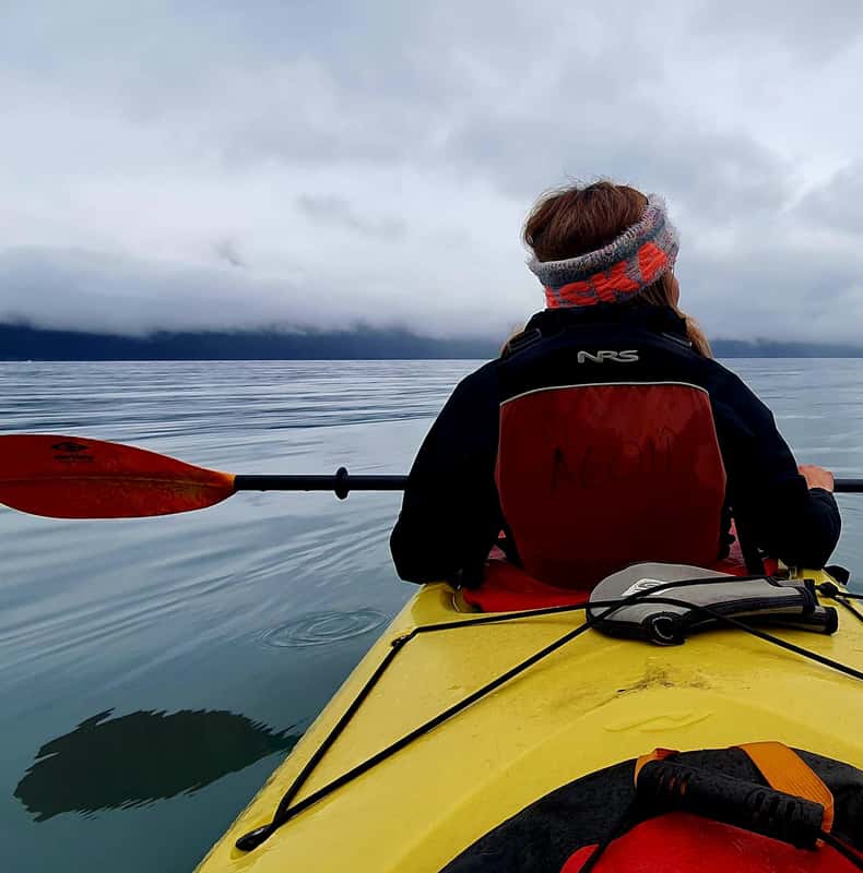 Blick aus einem gelben Kajak auf einen Paddler und die Küstenlandschaft