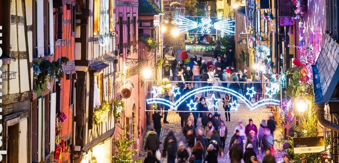 Crowds under Christmas light arches in an Alsace village street