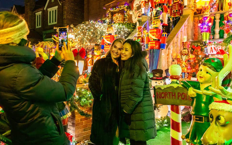 Two visitors posing for a photo in front of a North Pole sign and nutcrackers