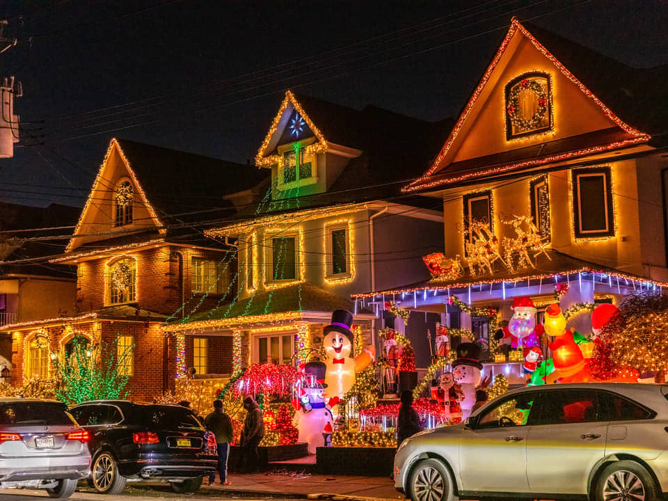 Lit houses with a snowman and parked cars on a residential street