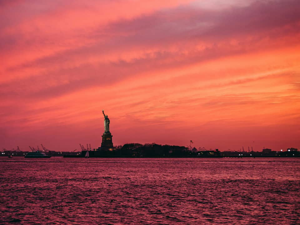 Statue of Liberty silhouette against a pink sunset sky