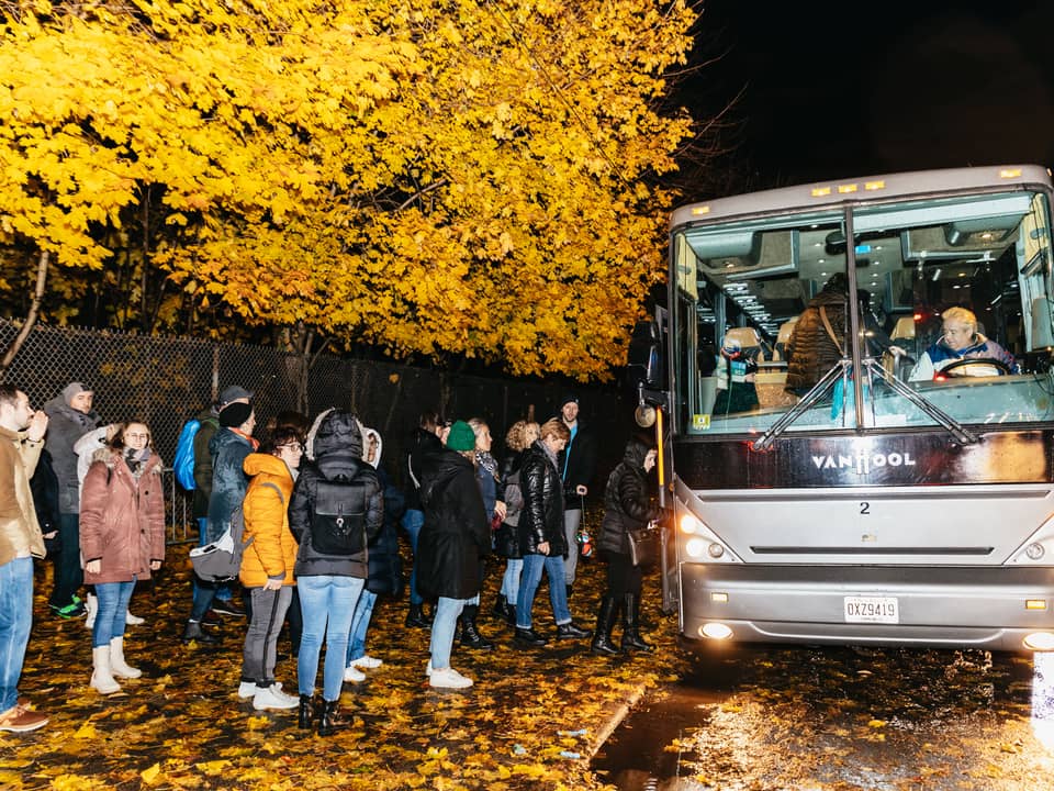 Tour bus and a group of visitors on a tree-lined street at dusk