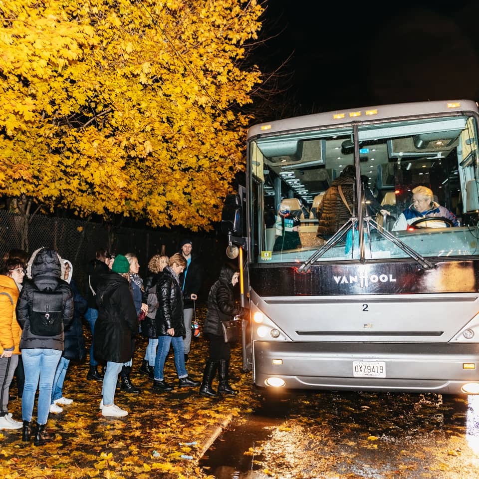 Tour bus and a group of visitors on a tree-lined street at dusk