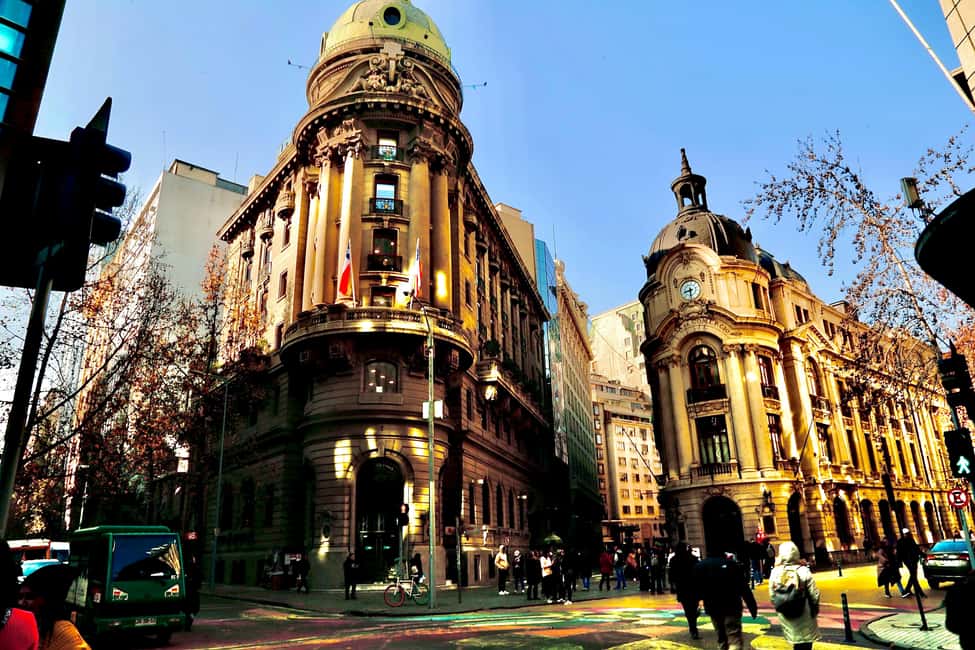 Historic buildings with intricate architecture in the center of Santiago, Chile, featuring a clear blue sky and pedestrians crossing the street.