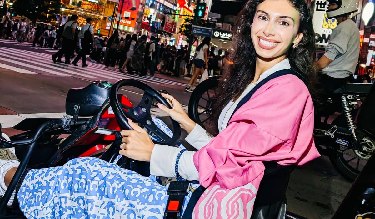 A smiling woman in a pink jacket at the wheel, with the Shibuya Crossing crowd behind her, by day. Photo from the operator's GetYourGuide listing.