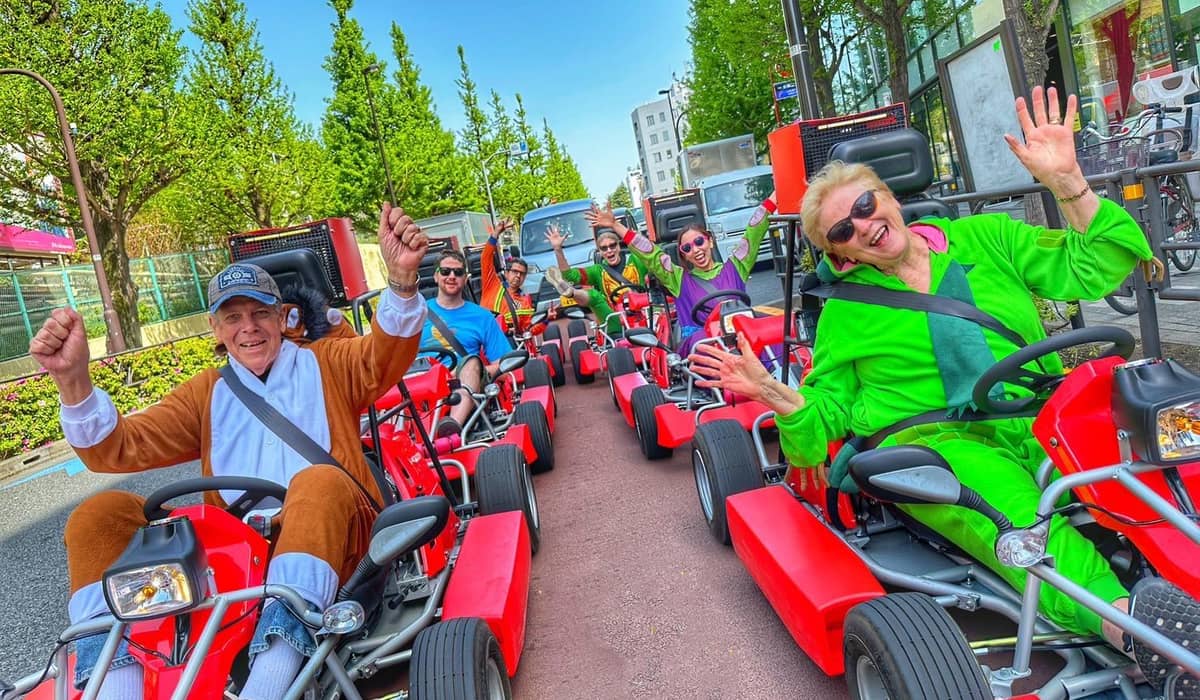 About eight red karts in a line on a wide avenue, drivers in bright costumes with arms up, spring greenery behind. Photo from the operator's GetYourGuide listing.