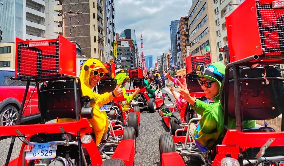 Red karts with rear boxes on a wide road, drivers in yellow, glass towers behind. Photo from the operator's GetYourGuide listing.