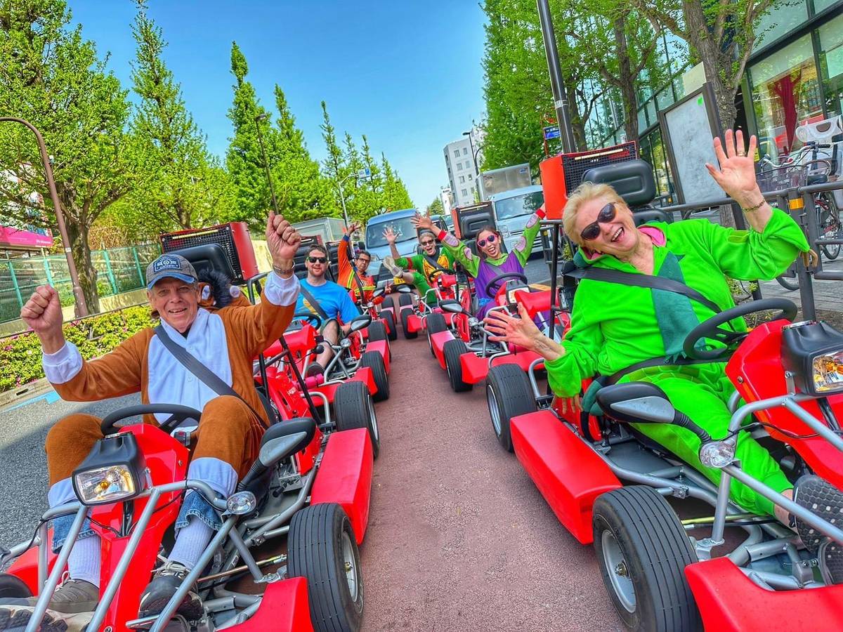 Red karts with waving drivers on a wide tree-lined avenue