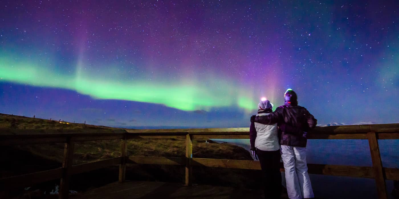 Couple at a wooden fence under a purple and green aurora, starry sky
